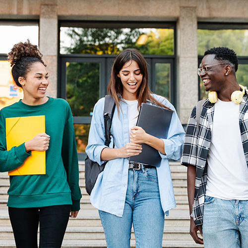 Happy students walking together on university campus, chatting and laughing outdoors after classes